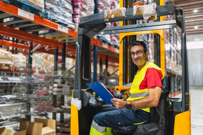 Forklift operator completing a daily forklift inspection checklist in a warehouse before shift start