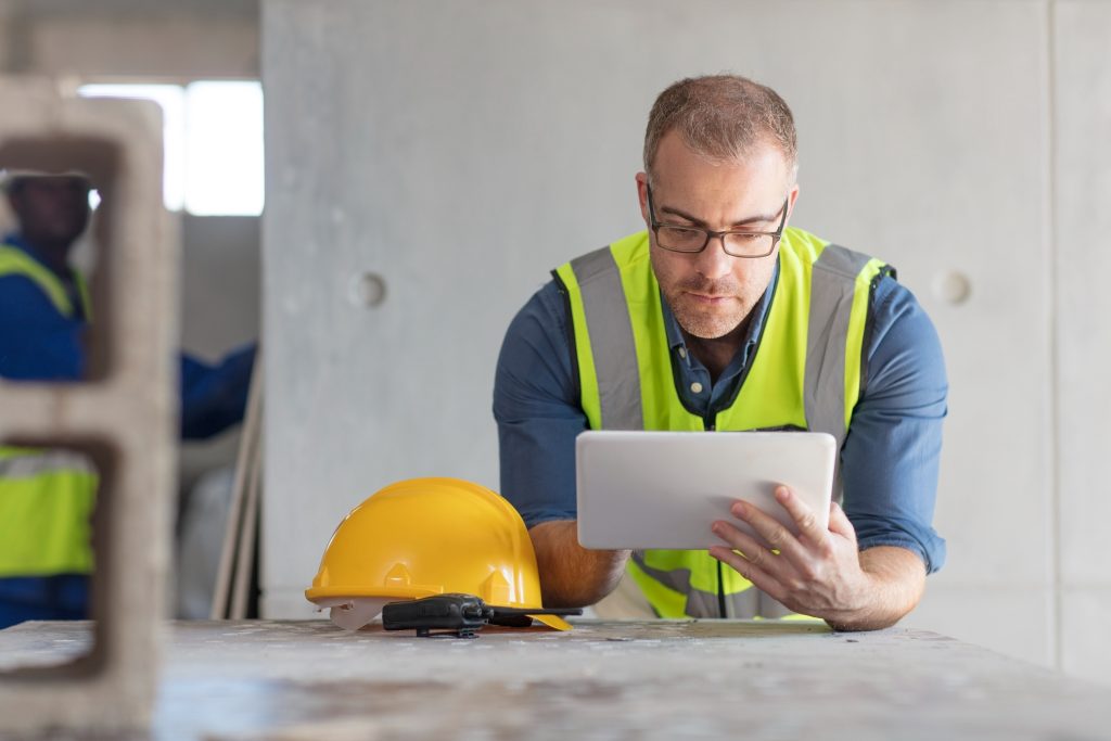 Site manager using a tablet on a construction site with a hard hat and radio on the table