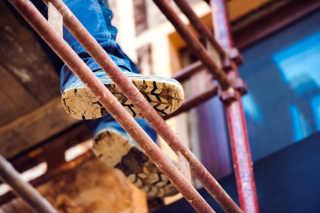 Worker's boots on scaffold tubes seen from below on a construction site