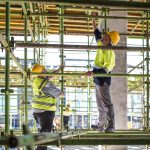 Two construction workers in hi-vis vests and hard hats checking scaffolding on a building site