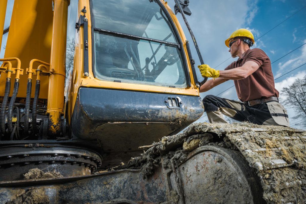 Worker in a hard hat and gloves opening the cab door of an excavator