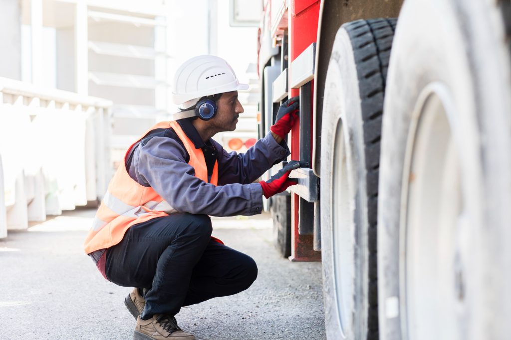 Driver in a hi-vis vest crouched beside an HGV wheel during a daily walkaround check