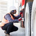 Driver in a hi-vis vest crouched beside an HGV wheel during a daily walkaround check
