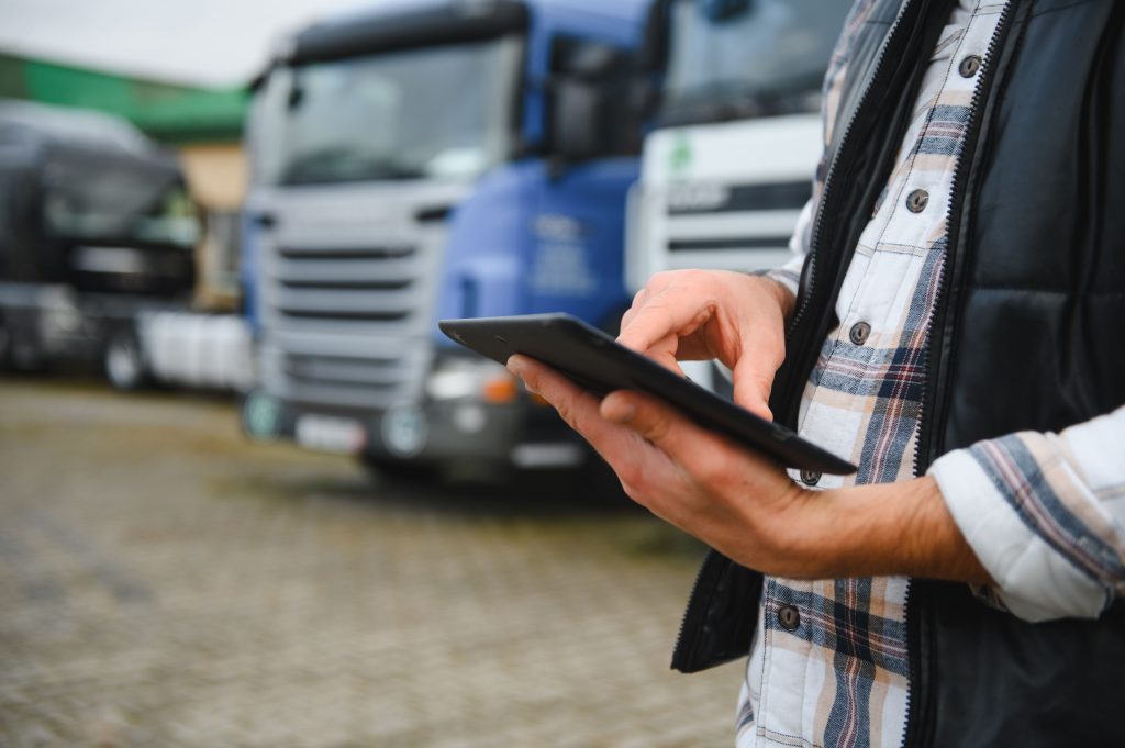 Transport manager using a tablet in front of parked HGVs at a depot