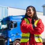 HGV driver in a hi-vis jacket standing in front of a lorry at a depot